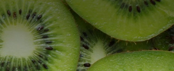 A tall glass of vibrant green kiwi and spinach smoothie next to fresh sliced kiwis on a kitchen table.