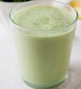 A tall glass of vibrant green kiwi and spinach smoothie next to fresh sliced kiwis on a kitchen table.